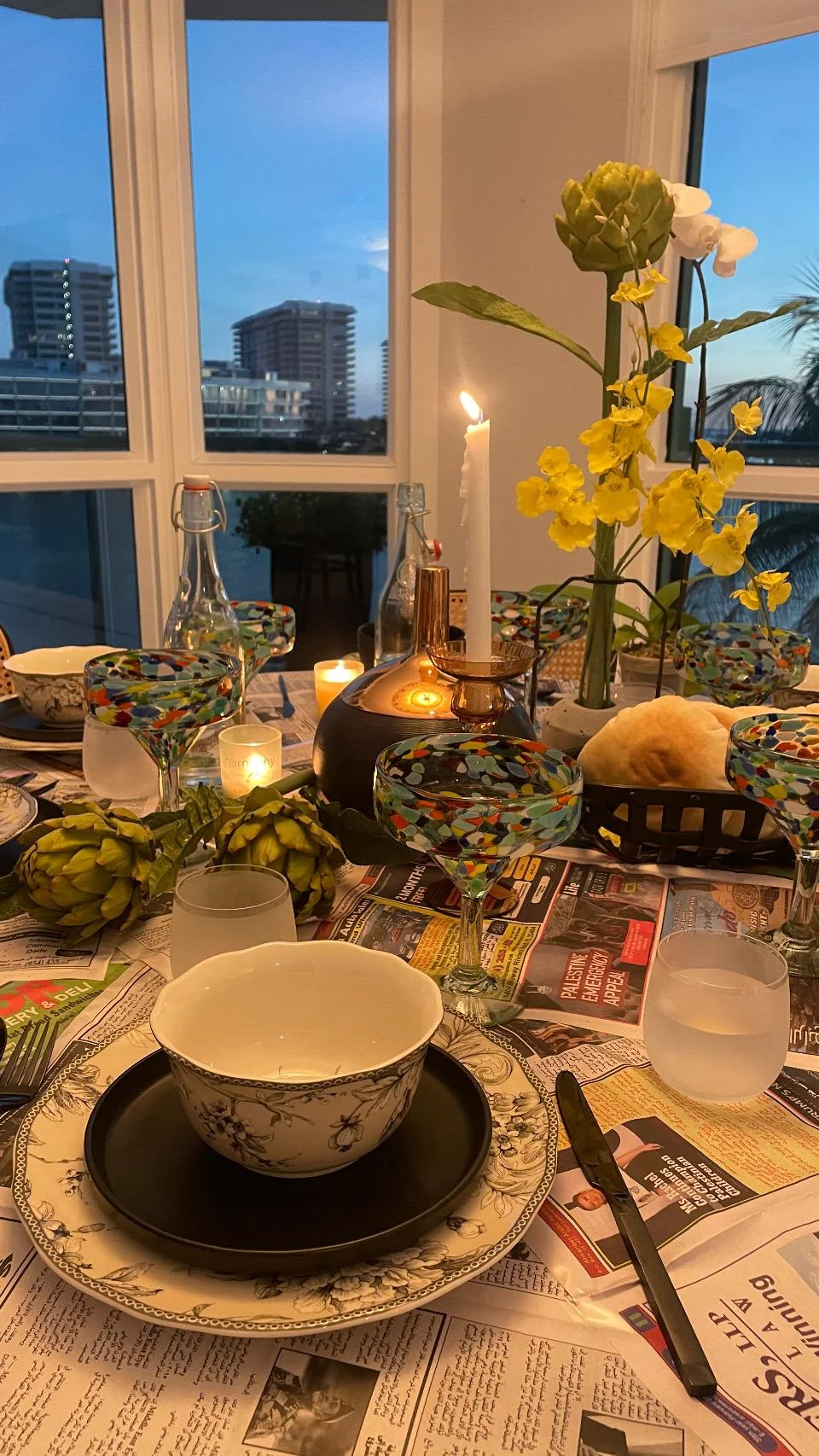 Mesa con mantel de periódicos, flores amarillas y copas multicolores