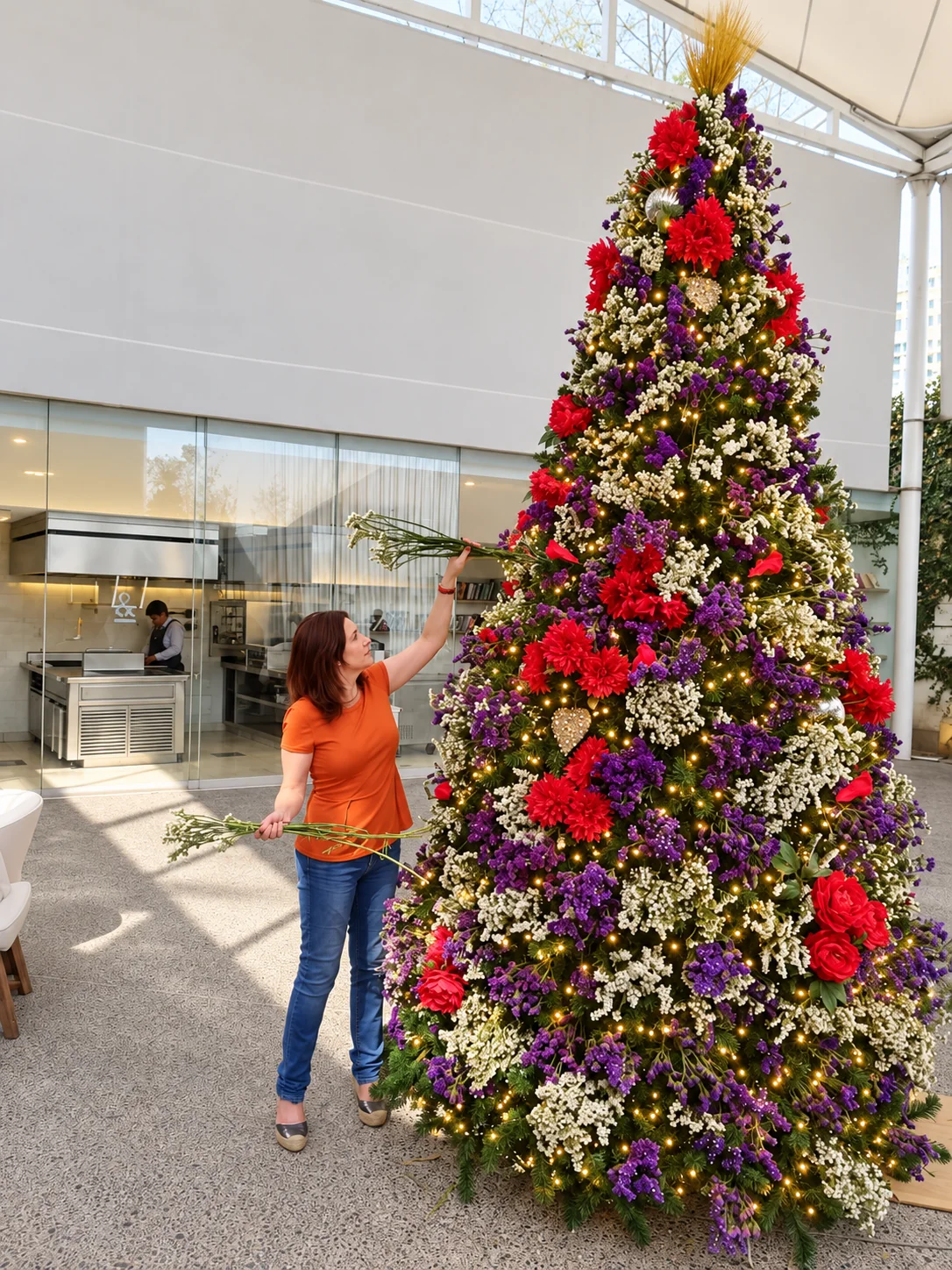 Karina Barhumi decorando un árbol monumental de flores rojas, moradas y blancas lleno de luces cálidas